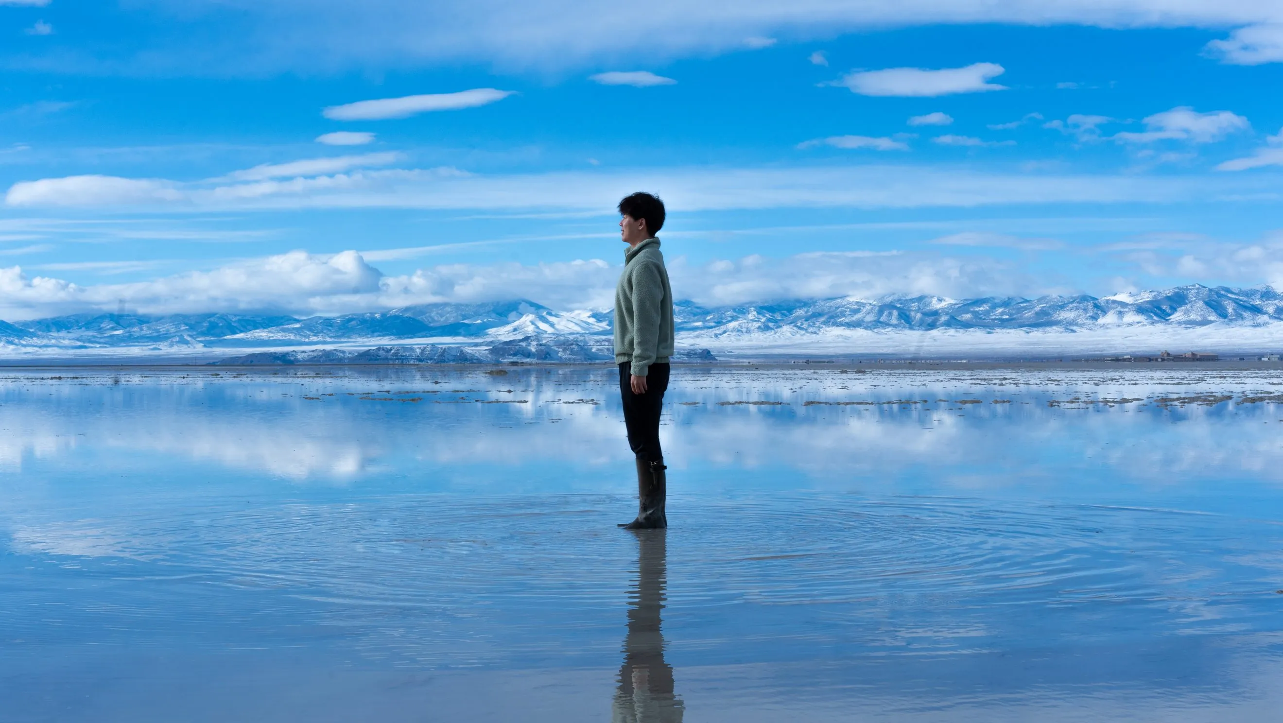 Jooyoung Joung standing in a mirror-like salt flat with snowy mountains behind